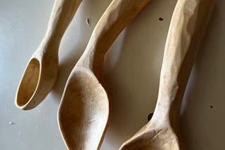 Three small, handcarved wooden spoons on a white tabletop.