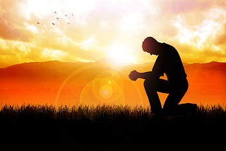 Man kneeling in grass against backdrop of a sunrise.
