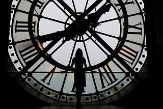 The silhouette of a tall woman stands at a large portrait window facing a clock