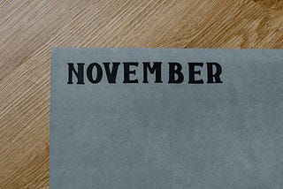 A sheet of paper on a table with “November” written in thick shaded pencil on it.