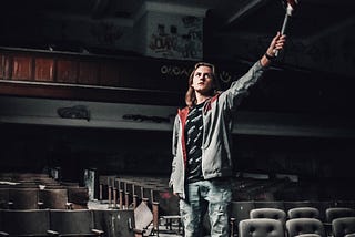 Young man waving an American flag in an old decaying empty theatre.