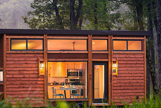 a tiny home with a rustic style exterior with a wooded backdrop on a dreary evening