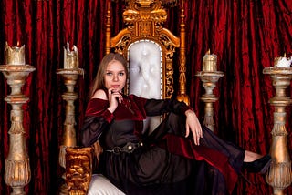 Medieval queen in an old style posing on golden throne in castle room
