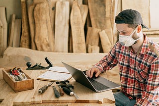 Carpenter working on his laptop surrounded by wood