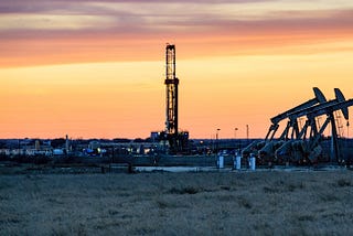 A fracking well and oil pumps are seen with a sunset in the background.