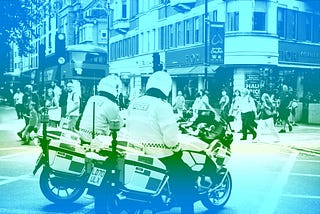 Police officers on motorcycles, parked on a city high street with a blue color overlay