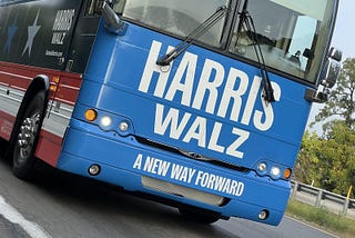 photo of the front of a Harris-Walz campaign bus on the road. text on the bus reads: Harris, Walz, A New Way Forward”