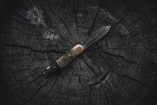 A black knife with a slightly worn-down black handle, in the middle of a wooden surface.