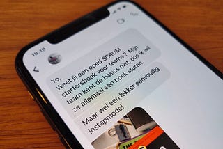 Dutch-language chat messages about Scrum books, displayed on the screen of the author’s iPhone, atop a wooden table