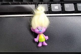 A happy purple troll doll with yellow hair wearing a dress, laying on a Windows keyboard.