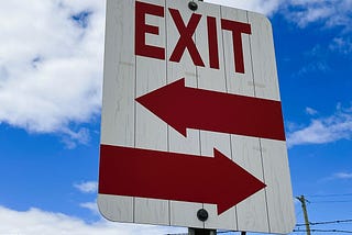 An exit sign that seems to indicate two possible passageways.