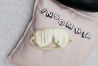 Pillow with Insomnia written on it, and a eye mask on top of it.