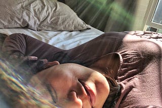 K. Asian American woman smiling with lips pursed and eyes close while basking in sunshine with sunspots in the photo