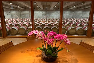 An orchid on a table with wine barrels behind the window