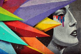 Progile black and white graffiti of woman crying with rainbow colored tears. She is peaking through rainbow colored spikes in the foreground.