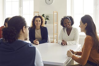 A multiethnic and diversive team around an table in the office talking and listening to each other. allyship and advocacy begins with with understanding and awareness.