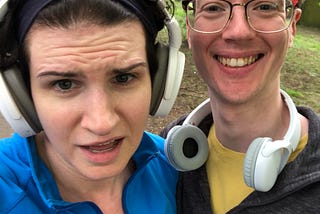 Two white people — on the left is a white, femme, white person wearing headphones and looking exasperated. On the right is a white man with glasses and headphones around his neck looking very happy.