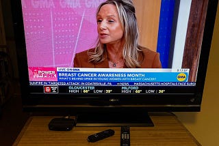 The photo shows a TV sitting on a small brown table. The remotes that control the TV are placed on the table before it. The TV displays the popular show Good Morning America.