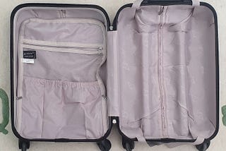 An image of an empty open suitcase on a rug. The suitcase lining is light grey. The dark grey exterior of the suitcase is just visible.