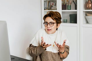 Woman with glasses and white and brown sweater shrugging to show how little she cares what men think about her.