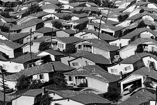 Vintage black-and-white photo of a densely populated suburban neighborhood of single-family homes. A wavy effect has been added to the photo.