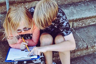 Two children on steps with a clipboard trying to figure something out together.