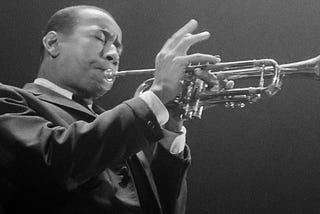 Lee Morgan, an African American man, is wearing a suit and playing a trumpet