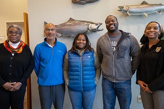 Five employees take a group photo in an office. They have fish on the walls behind them.