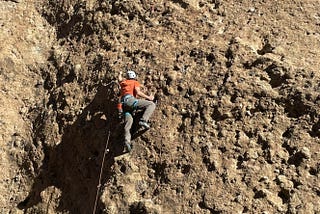 Climber ascends a rugged rock face, showcasing determination and skill.