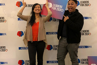 A man and woman holding props in front of a backdrop of Leaders for 2030