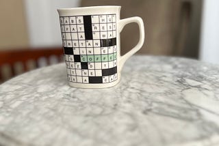 Picture with a coffee cup that has an image of a crossword puzzle printed on it.