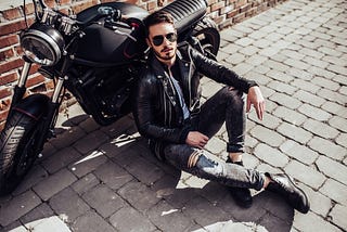 A man in leather sitting, leaning on a motorbike