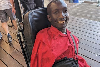 Isaac, smiling in his wheelchair, with people walking in the background.