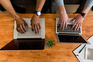 A photo of two people’s hands working on two laptop computers side-by-side.