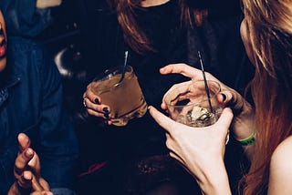 duas mulheres se divertindo numa festa com bebidas na mão. a imagem está cortada e mostra apenas o sorriso de uma delas.