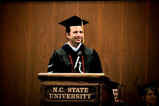 The author, wearing doctoral regalia and a graduation cap, stands behind an N.C. State University podium while giving a commencement address in 2009, the same year he earned his PhD.