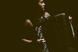 A woman playing a button accordion in moody dark lighting