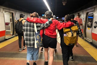 Mack Lawrence and two friends walking on a subway platform in New York City. Image taken from the back.