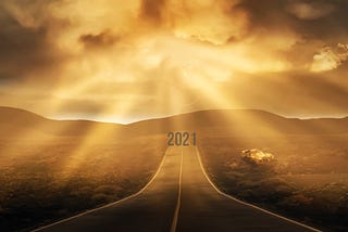 Two way road on the horizon with sunlight shining from cloud and the words 2021 at the end of the road.