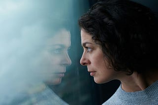 Mid aged woman staring out window, seeing her reflection