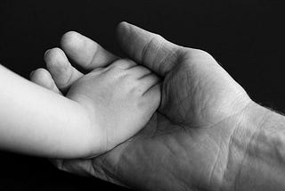 Black and white photo of an adult hand cradling the hand of a small child