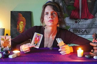 Psychic Reader, Rozalia Kieliszkiewicz holding the Justice Major Arcana Tarot Card with a Buddha and Libra picture in the background.