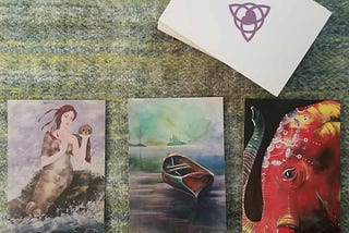 3 upturned Oracle cards showing a Selkie, a boat, and an elephant placed horizontally below to the rest of the deck in a stack