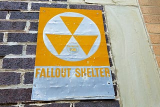 A fallout shelter sign is posted on the side of a brick building.