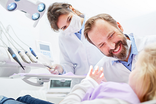 Stock image of a child in a dentist’s chair with a dentist and dental hygienist smiling while conversing with the child.