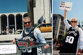Regis Philbin standing in front of the Lincoln Center wearing a David Robinson 50 jersey and holding a San Antonio Spurs Banner with the Statue of Liberty in the background.