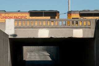 Two yellow partially-seen Union Pacific locomotives crossing an old beaten-up-looking grey concrete bridge.