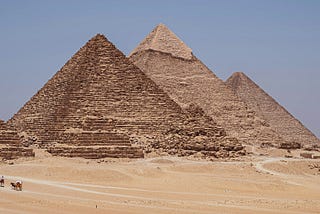 An image of the great Pyramids, with a camel train in the foreground.