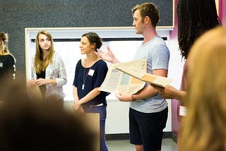 Project Wayfinder’s CEO/Founder, Patrick Cook-Deegan, holding a Purpose Toolkit while talking in a circle with students and teachers. The background is a school classroom with a large white board.