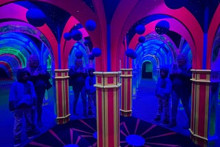 Me and my kiddo at the Infinite Mirror Maze on Pier 39, looking in many mirrors with lots of black-light arches and mirrors!